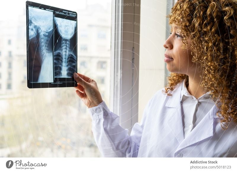 Crop ethnic doctor analyzing radiographic image of backbone in clinic analyze x ray radiography attentive woman office portrait medic spine diagnostic study