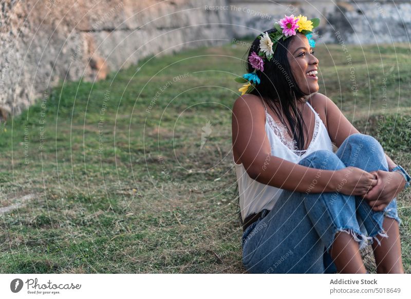 Smiling ethnic woman in floral wreath in field flower serene romantic charming embracing knee gentle female nature tender calm summer feminine meadow delicate