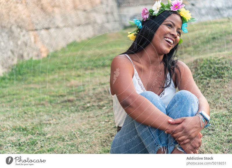 Smiling ethnic woman in floral wreath in field flower serene romantic charming embracing knee gentle female nature tender calm summer feminine meadow delicate