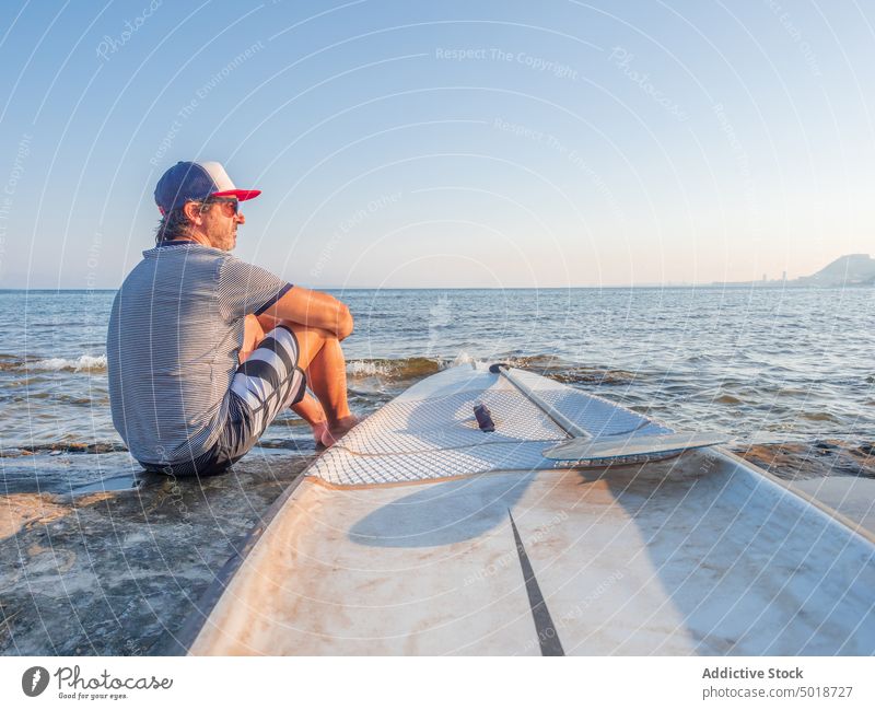 Mature man with surfboard on coast in water beach seaside summer vacation sport ocean surfer lifestyle leisure recreation active sand hobby adult swimwear