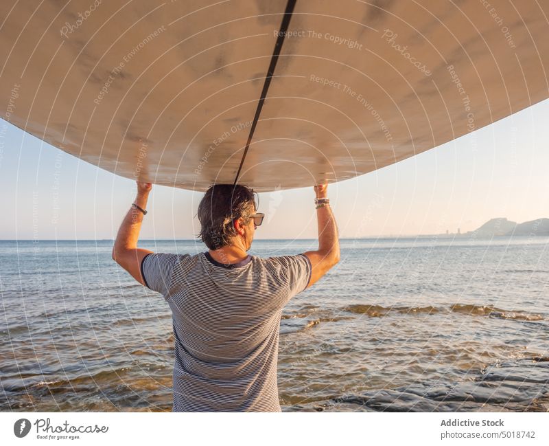 Man holding surfboard over head and looking along man seaside summer vacation water beach sport ocean surfer lifestyle leisure recreation active sand hobby