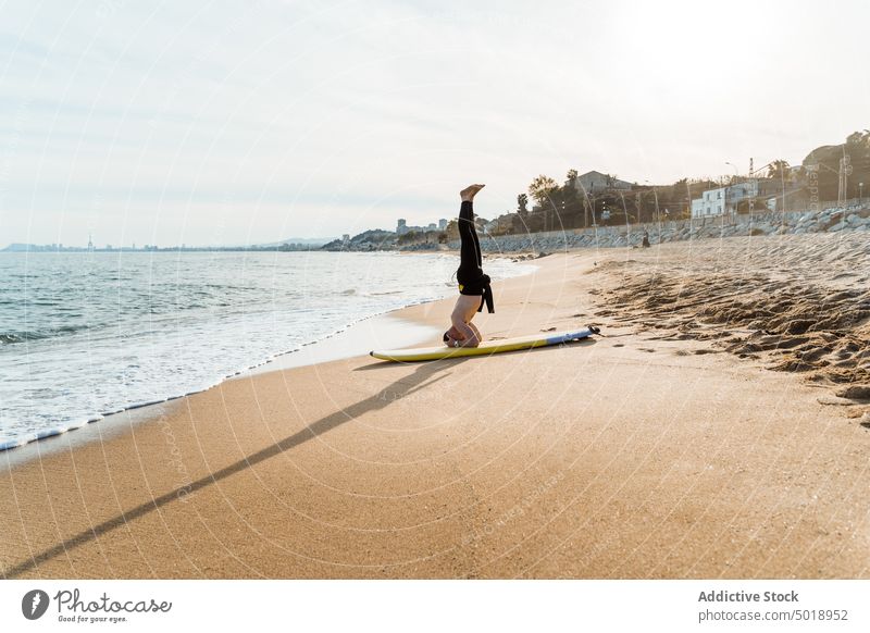 Surfer doing handstand on beach surfer man surfboard headstand sea wave active sporty exercise summer ocean shirtless male young shore seashore activity sand