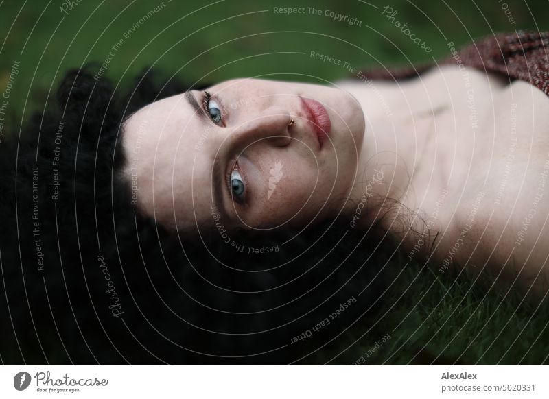 Close portrait of young dark haired woman with curls, light blue eyes and freckles lying in grass Woman Young woman Freckles Curl Brunette long hairs pale