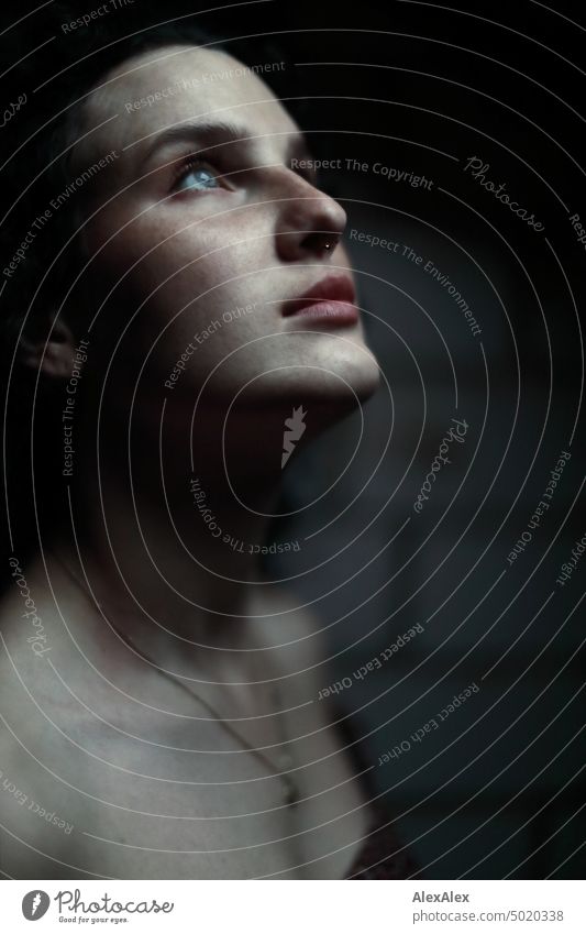 Close up of dark side portrait of young woman with long dark curly hair and freckles in dark room - she looks up to sparse light Woman Young woman Freckles Curl