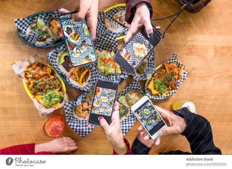 Crop faceless friends taking photos of food in restaurant take photo smartphone obsessive habit food photography meal blogger gather together delicious device