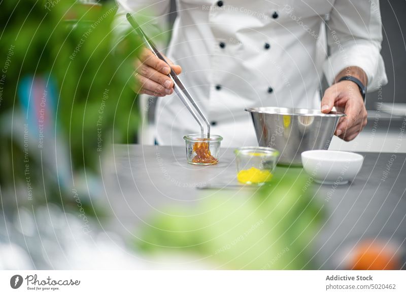 Unrecognizable chef cooking food with tongs near ingredients in jars man kitchen table process mix male prepare professional recipe glass job uniform delicious