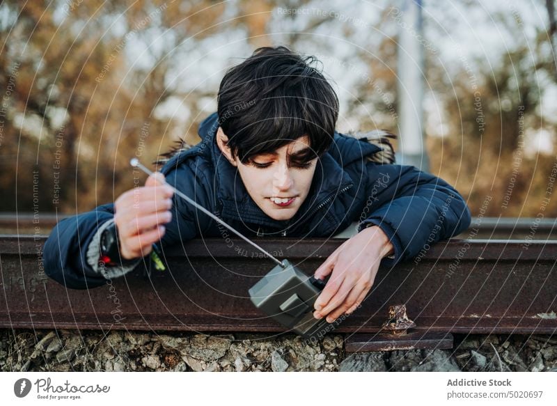 young child holding a walkie-talkie lying on train tracks boy male communication playground playing green children portrait blue radio cute fun childhood