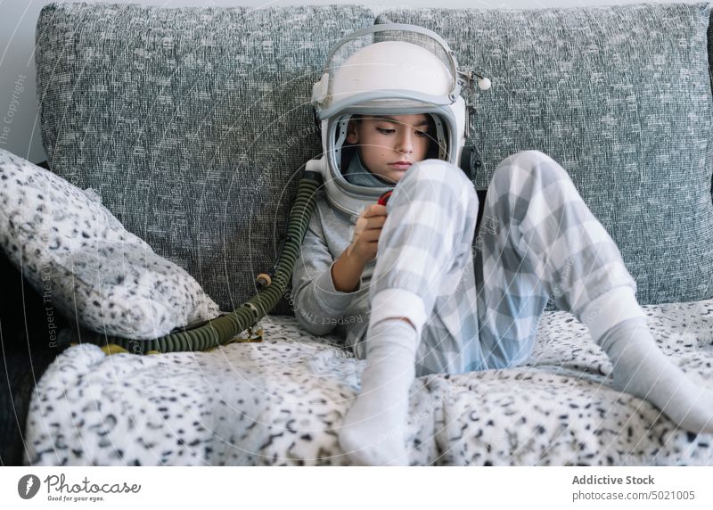 Kid lying on couch and playing with a video game console at home astronaut background boy child childhood concept costume creation handmade helmet imagination