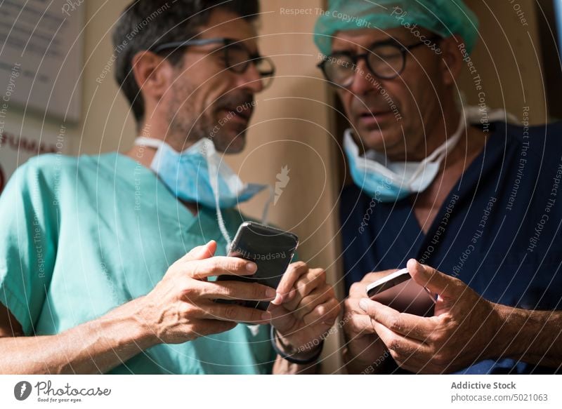 Surgeons using smartphones together surgeons hospital office doctors clinic healthcare men team uniform medicine technology device gadget browsing social media