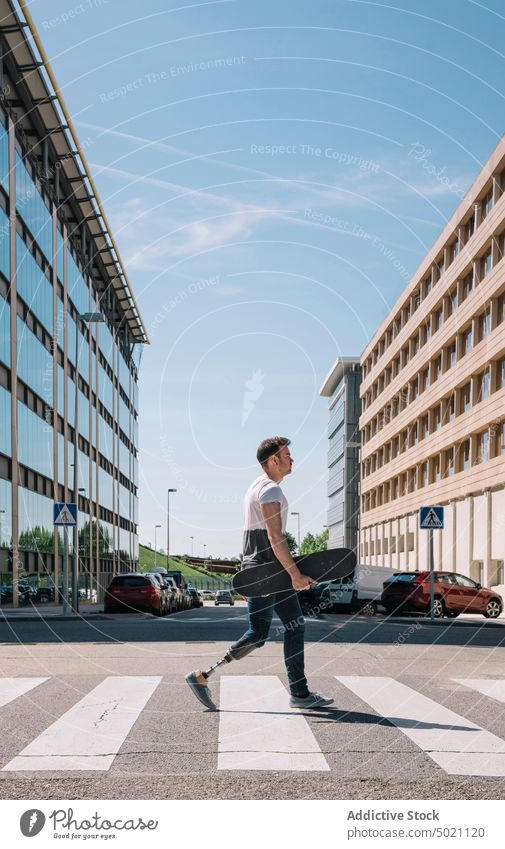 Skater with leg prosthesis crossing road man skateboard crosswalk artificial motivation street strong city young urban male carrying modern sunny daytime hobby