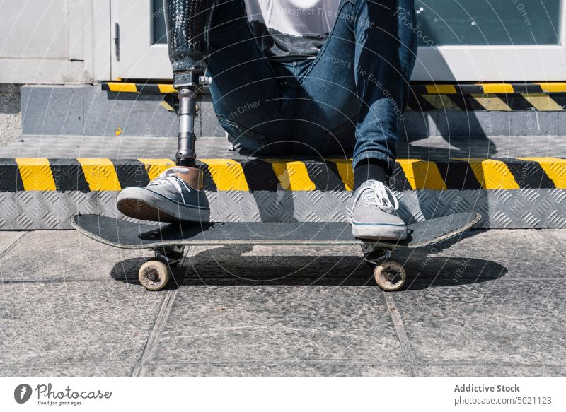 Crop skater with leg prosthesis sitting on stairs man skateboard artificial street city young urban male modern sunny daytime break hobby handicapped guy limb