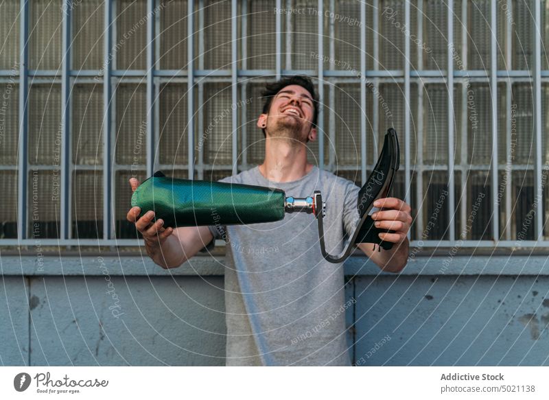 Cheerful guy showing artificial leg man street city acceptance strong smile laughing disabled urban building wall male challenge happy determination cheerful