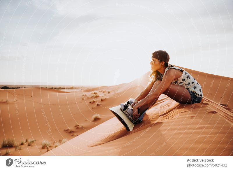 Young woman sitting on sand ready for sandboarding sport extreme desert lifestyle leisure fun vacation female travel holiday tourism dry dune enjoyment prepare