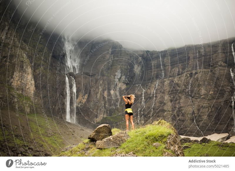 Anonymous female traveler near cliff with waterfall woman mountain rock trip overcast cloudy nature landscape pyrenees monte perdido tourist stone picturesque