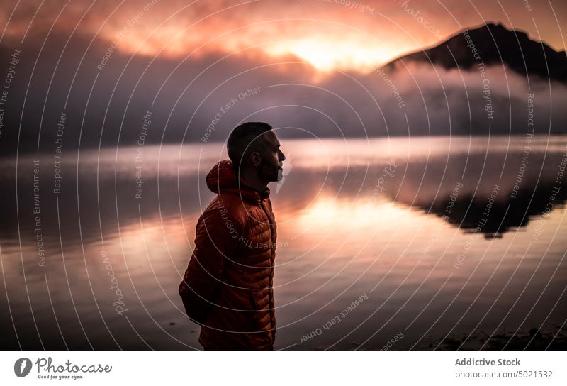 Male traveler contemplating sunset near mountain lake man alone nature reflection contemplate calm peaceful male tranquil relax thoughtful landscape water sky