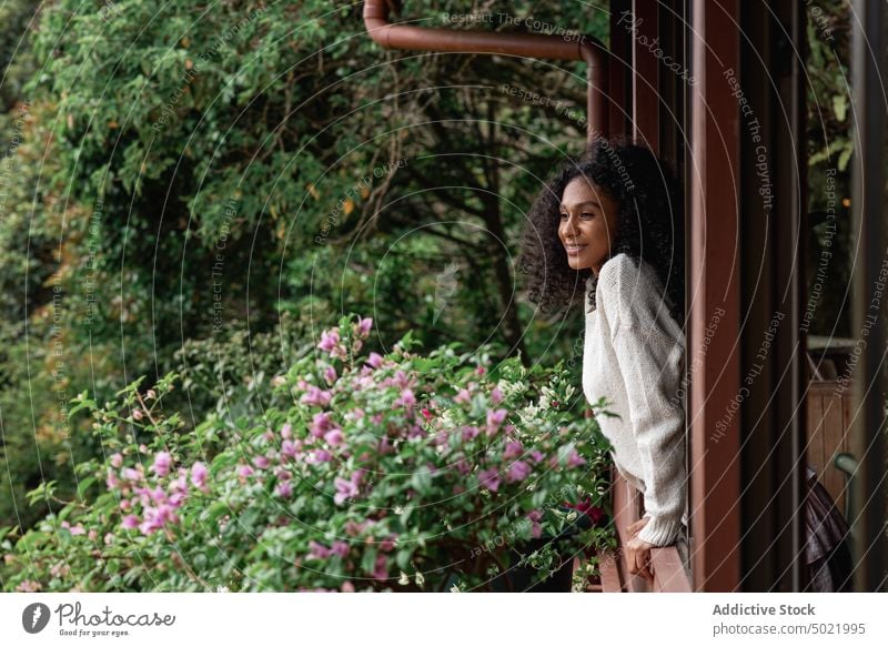 Smiling black woman against lush trees smile nature environment vegetate flower house village enjoy admire contemplate shrub flora bloom content charming