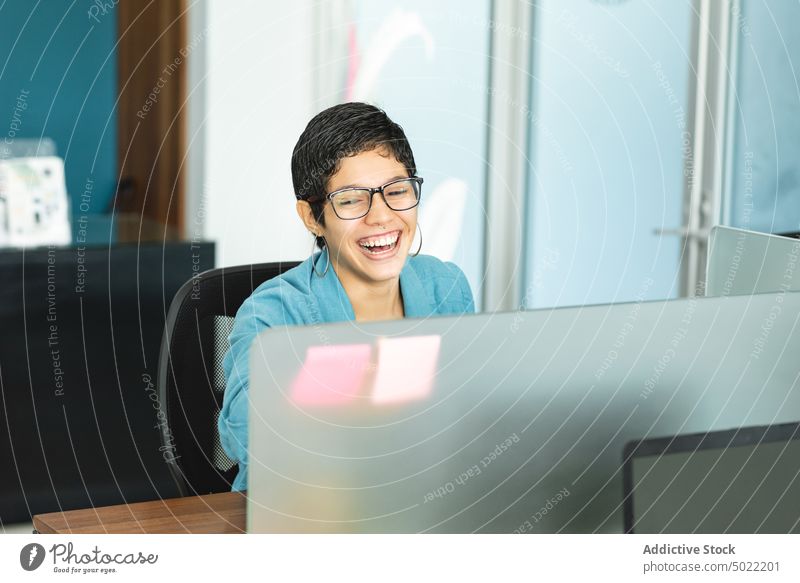 Happy ethnic woman sitting at table with laptop during work in office cheerful entrepreneur using laugh positive job female hispanic costa rica america style