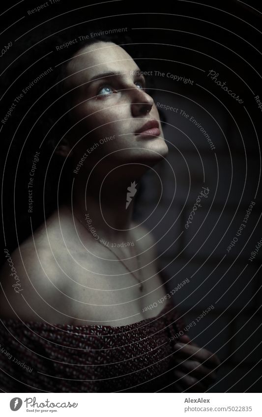 Close up of dark side portrait of young woman with long dark curly hair and freckles in dark room - she looks up to sparse light Woman Young woman Freckles Curl