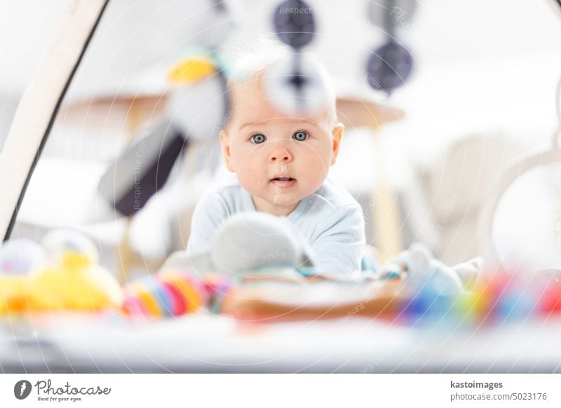 Cute baby boy playing with hanging toys arch on mat at home Baby activity and play center for early infant development. Baby playing at home newborn childhood