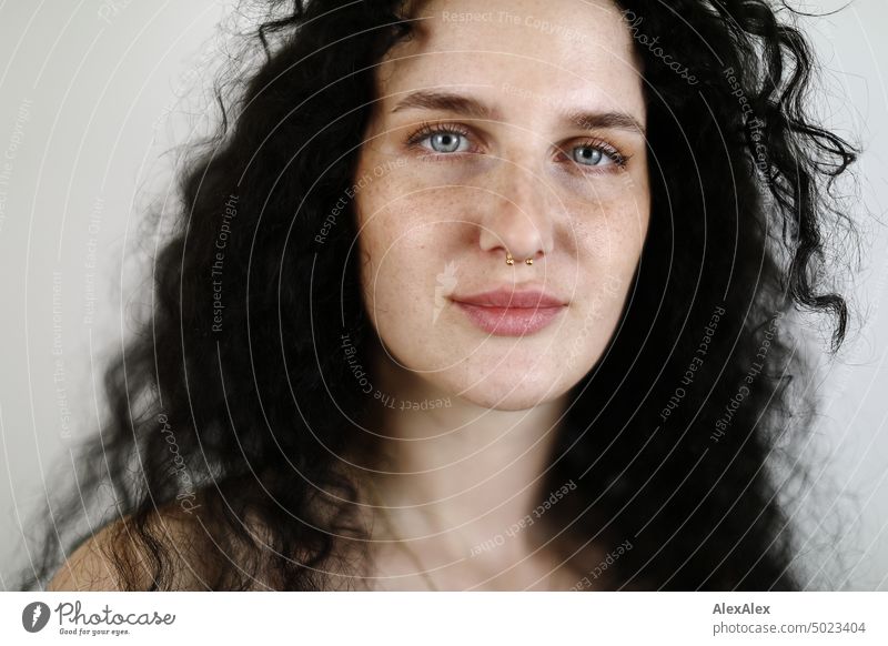 Close portrait of young dark haired woman with curls, light blue eyes and freckles in front of white wall Woman Young woman Freckles Curl Brunette long hairs