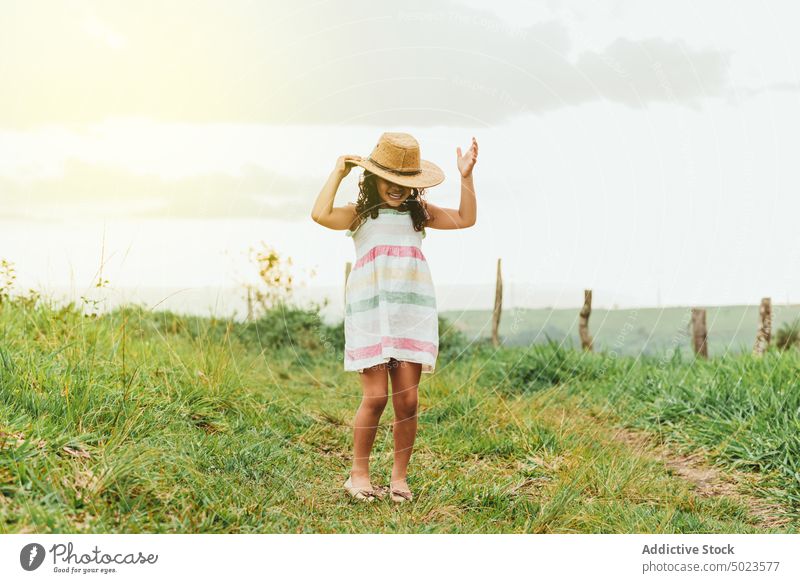 Cheerful girl in grassy field morning countryside happy smile rest weekend summer kid meadow child nature joy cheerful glad dress hat touch head carefree