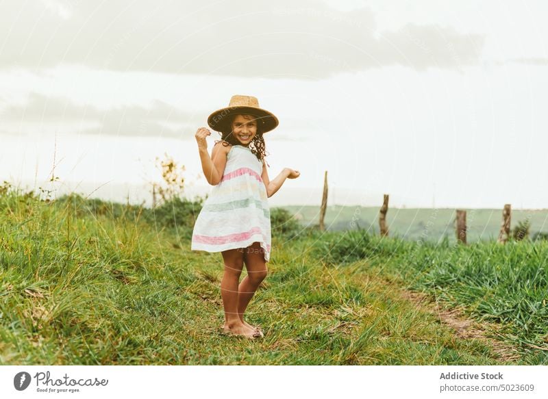 Cheerful girl in grassy field morning countryside happy smile rest weekend summer kid meadow child nature joy cheerful glad dress hat touch head carefree