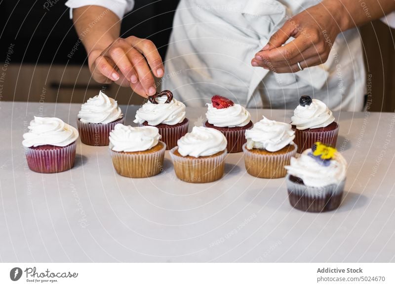 Anonymous baker decorating cupcakes at table bakery decorate berry woman bakehouse sweet dessert vegan female kitchen counter pastry baked culinary gastronomy