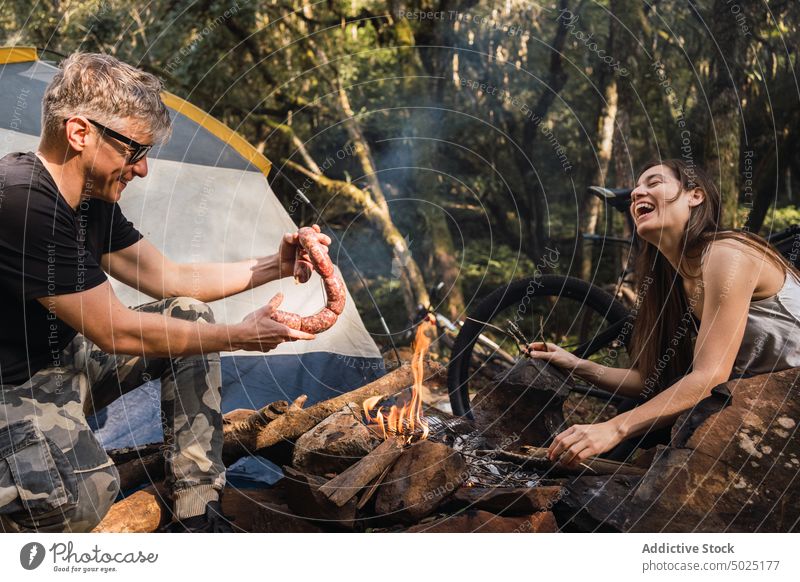 Hiker putting fresh sausages on rack over burning fire hiker prepare barbecue grill beef campsite man natural raw weekend product protein uncooked bbq campfire