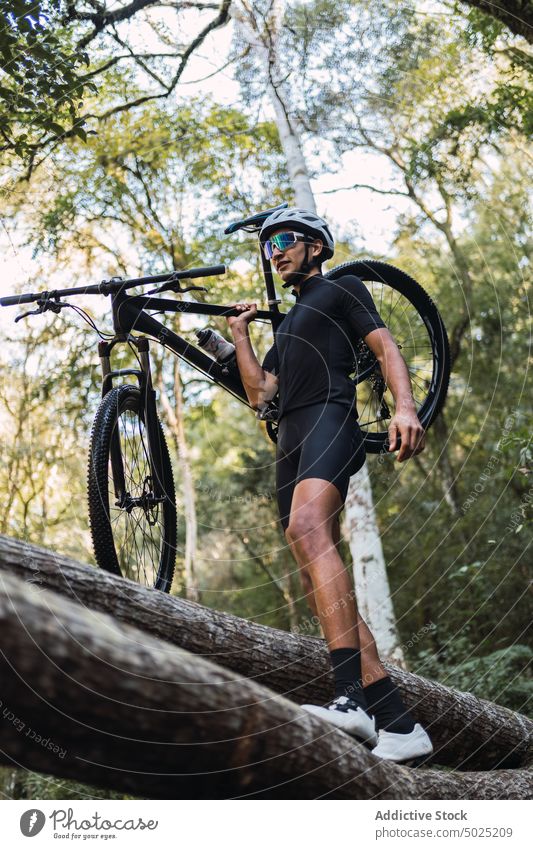 Cyclist with bike walking on fallen tree trunk in forest bicyclist balance sport danger fearless man woods stroll adrenalin extreme brave courage cycle bicycle