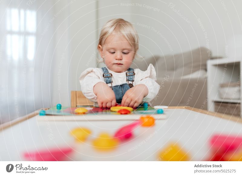 Cute girl playing board game at home assemble piece stare childhood charming portrait toddler innocent sweet table intent gaze denim sit friendly gentle stupor