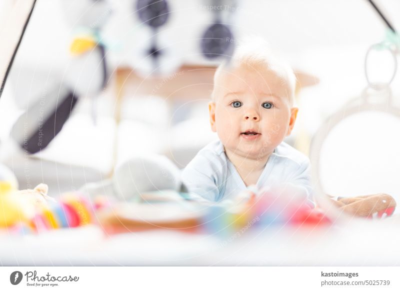 Cute baby boy playing with hanging toys arch on mat at home Baby activity and play center for early infant development. Baby playing at home newborn childhood