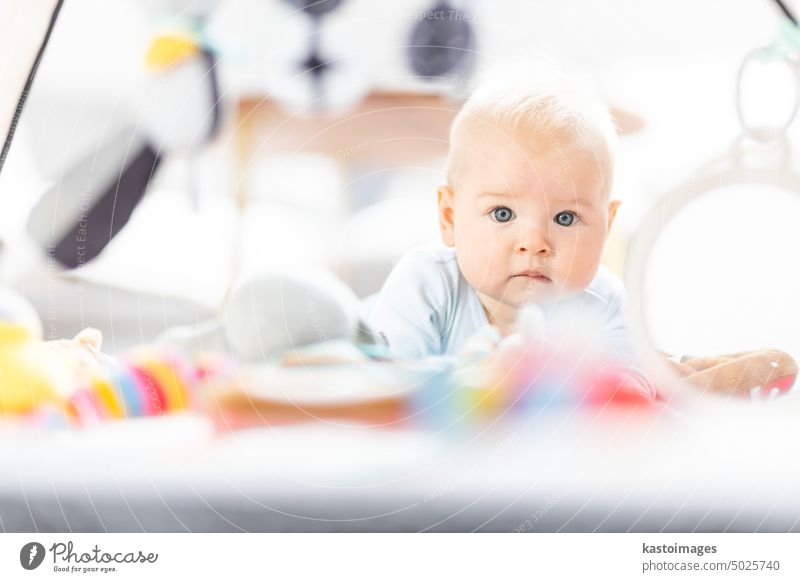 Cute baby boy playing with hanging toys arch on mat at home Baby activity and play center for early infant development. Baby playing at home newborn childhood