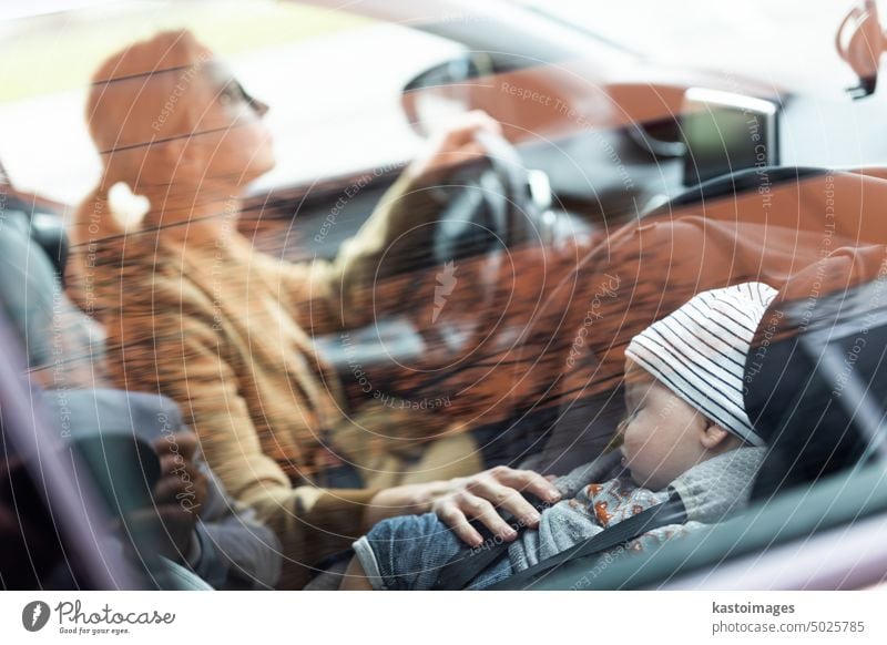 Mother concentrating on driving family car running errands while her baby sleeps in infant car seat by her site. mother drive child safety vehicle travel boy