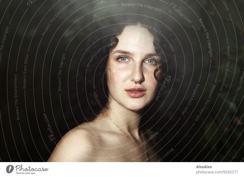 Close portrait of young dark haired woman with curls, light blue eyes and freckles - ivy can be seen in background Woman Young woman Freckles Curl Brunette