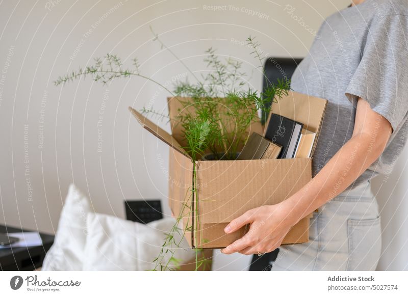 Crop woman carrying carton box with belongings relocate book plant potted home female casual apartment move in cardboard new property mortgage package container