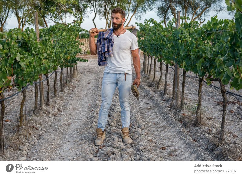 Serious young ethnic male farmer standing on agricultural plantation man field countryside agriculture rural work agronomy hispanic brunet job vineyard beard