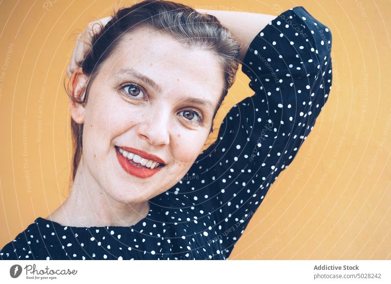 Confident woman smiling in yellow studio smile self assured touch hair coquette happy style cheerful portrait delight positive female young brunette red lips