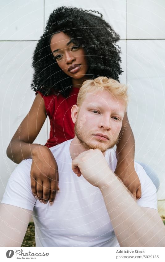 Unemotional diverse couple embracing near wall boyfriend girlfriend unemotional emotionless hug embrace relationship tile appearance together serious young calm