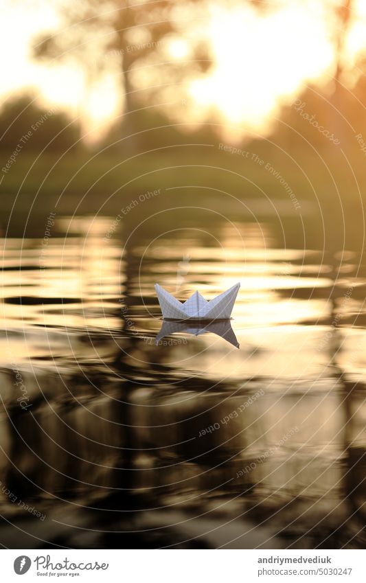 A paper boat is floating on the waves in the water at a beautiful sunset. Origami ship Sailing. The concept of a dream, future, childhood, freedom or hope. sea