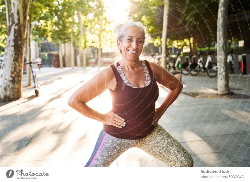 Smiling senior sportswoman exercising at street athlete smile exercise training fitness workout park lunge outside wellbeing sporty healthy sportswear wellness