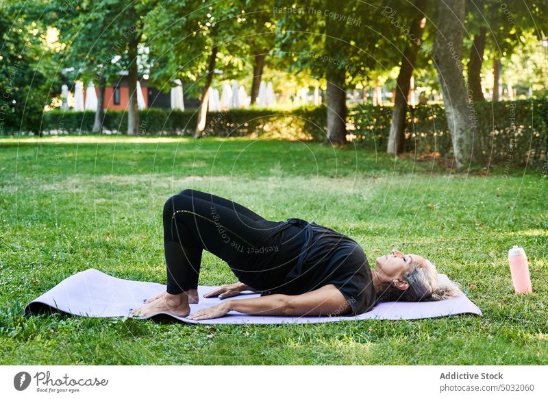 Aged female doing Bridge pose in park woman yoga session lawn mat bridge pose practice summer zen elderly senior aged asana vitality wellness wellbeing energy