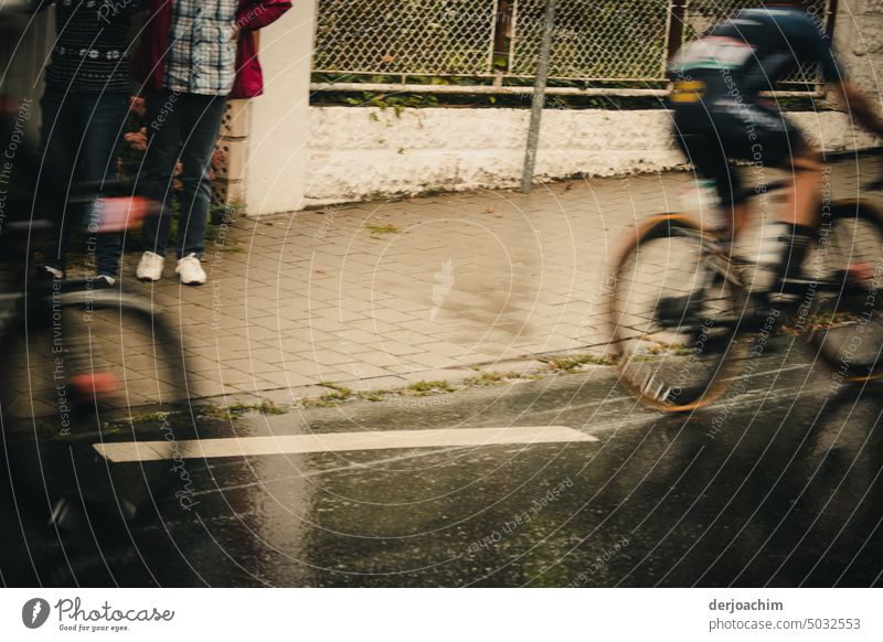 An exciting bike race through the city. The cyclists almost fly by. A few spectators watch this from a house entrance. Cycle race Colour photo Street Cycling