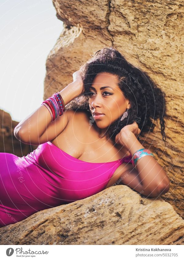 Portrait of cheerful black people, pretty happy young african american woman smiling. Rocks beach. Sexy girl in pink swimsuit and jewelry enjoying nature. Travel, holiday concept.