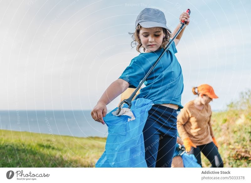 Cute girl picking up garbage for environment campaign volunteer collect trash plastic stick nature pollute ecology waste recycle summer litter rubbish