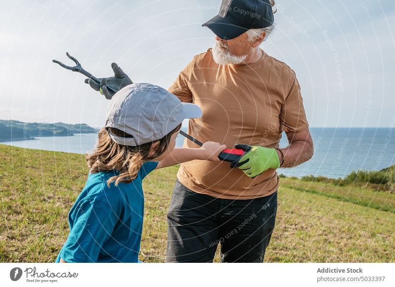 Grandfather and granddaughter collecting waste on field grandfather volunteer pick garbage trash nature kid man environment protect sunlight ecology bin rubbish