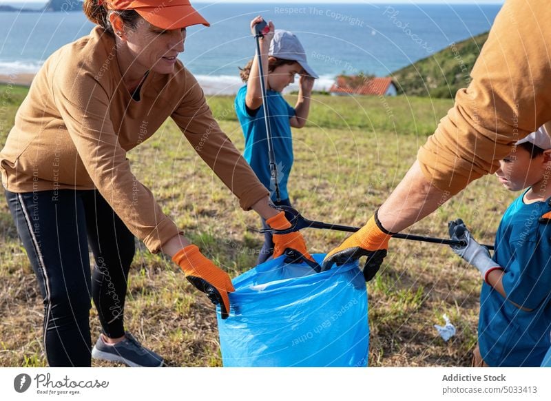 Family with kids collecting garbage together on field family volunteer ecology environment pick thrash tongs eco friendly hill sea recycle nature litter waste