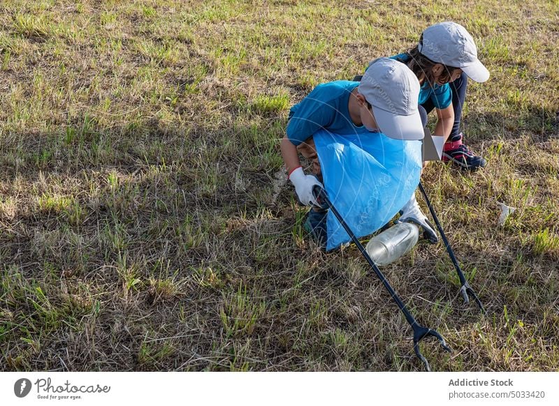 Kids with thrash tongs collecting garbage children volunteer waste litter plastic lawn grass environment ecology eco friendly pollute summer trash nature