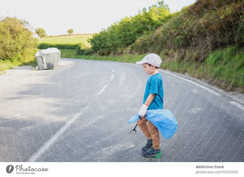 Boy with bin bag walking across road boy kid asphalt garbage trash glove volunteer trash tongs ecology child rubbish recycle litter care outside eco friendly