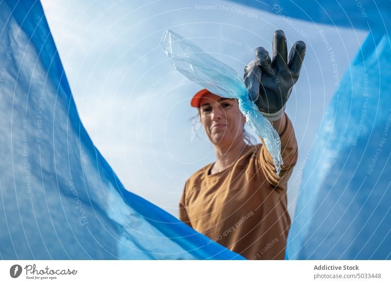 Positive woman throwing trash into bin bag volunteer positive garbage waste ecology environment recycle rubbish litter female glove protect cap pollute smile