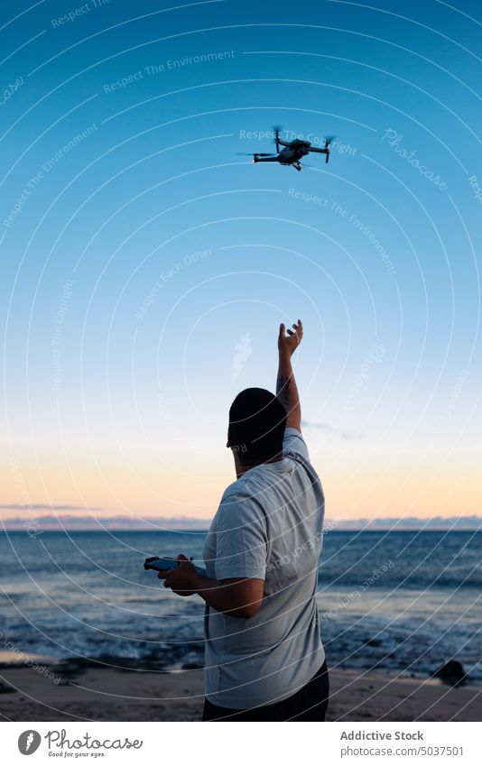 Black man launching drone near sea beach sunset sky wave summer traveler male ethnic black twilight dusk ocean coast evening seaside shore marine lifestyle